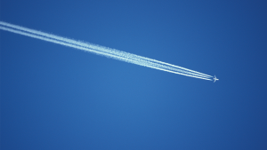 underside view of aircraft flying in blue sky with jet stream