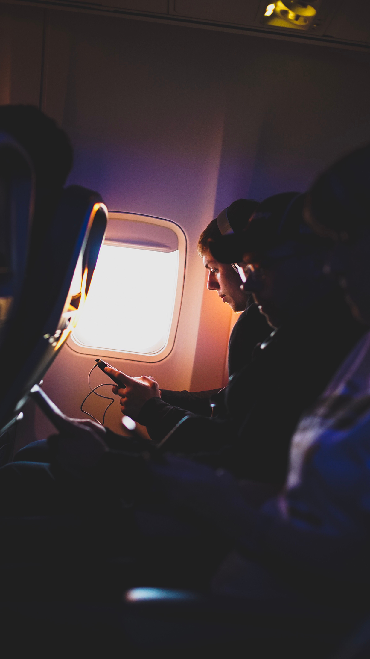 row of three people listening to music on airplane